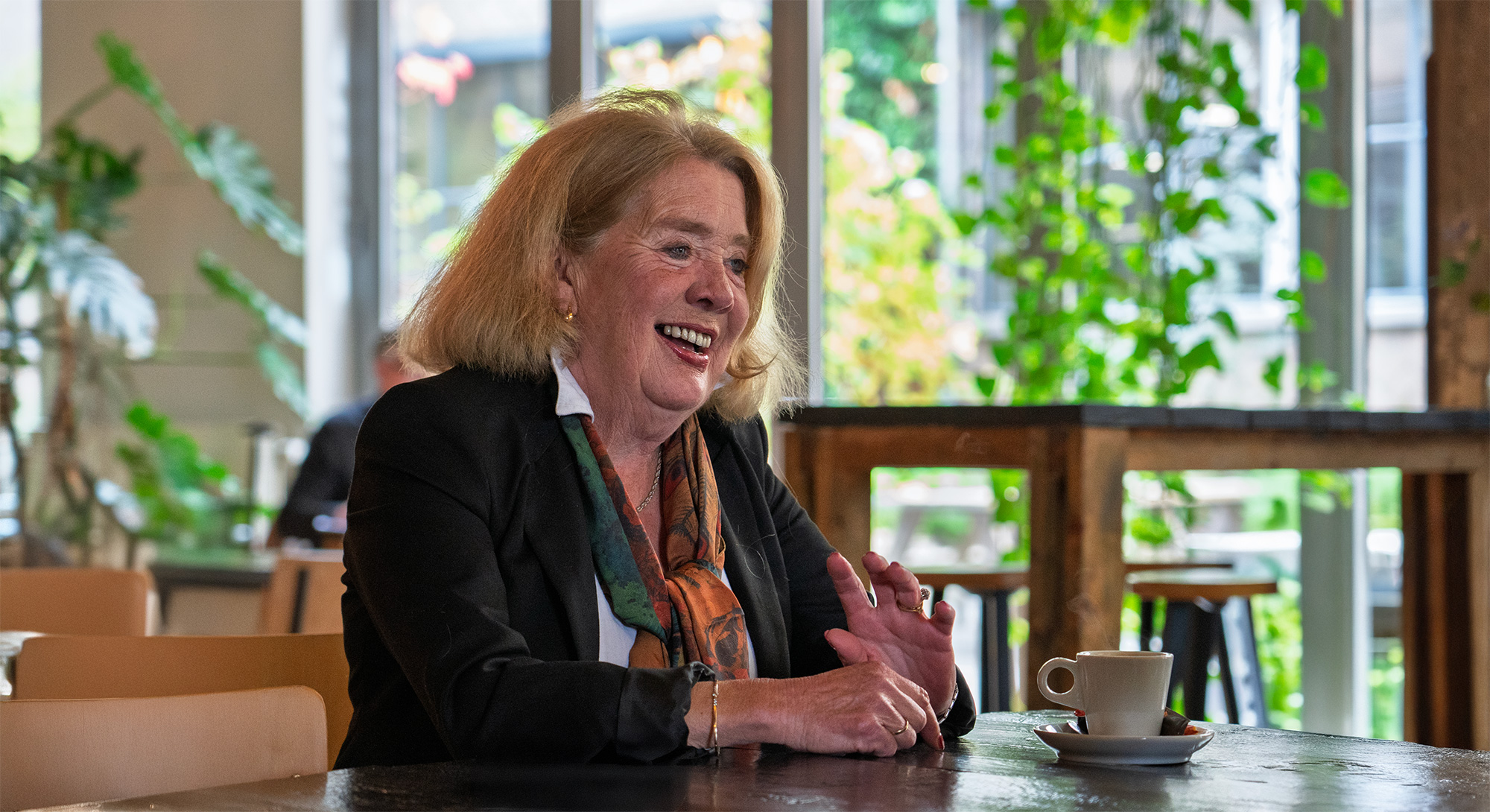 Marike zit glimlachend aan tafel met een kopje koffie