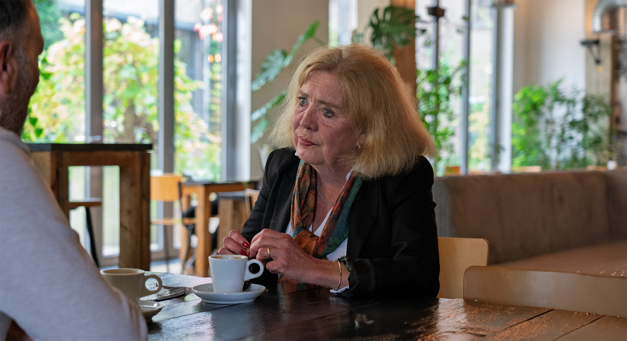 Marike zit glimlachend aan tafel met een kopje koffie